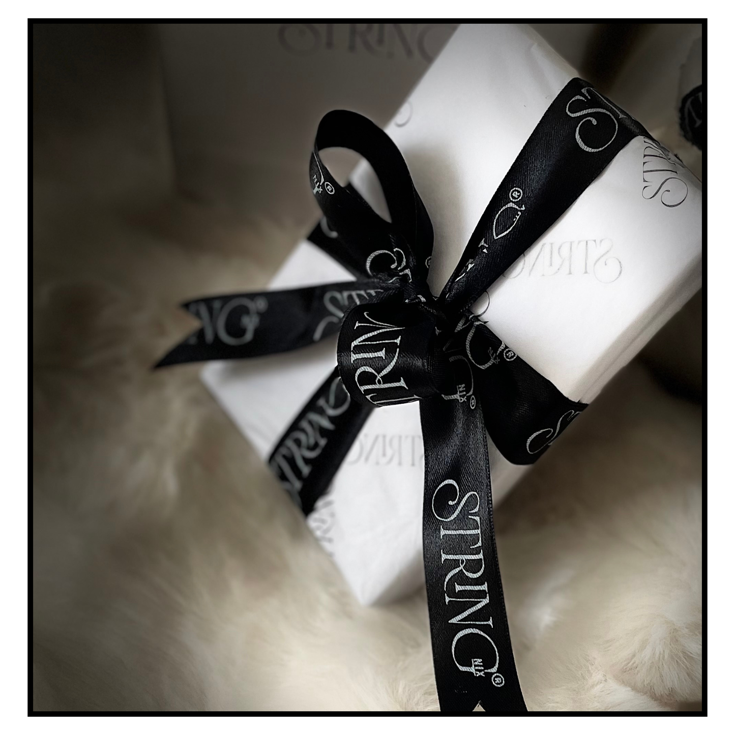 White string nix box wrapped with a black ribbon featuring 'STRING' branding on a soft surface.