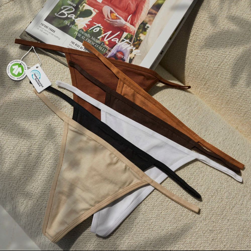 String Nix seamless thong underwear in assorted neutral shades, with sustainability tags, displayed on a magazine and fabric surface