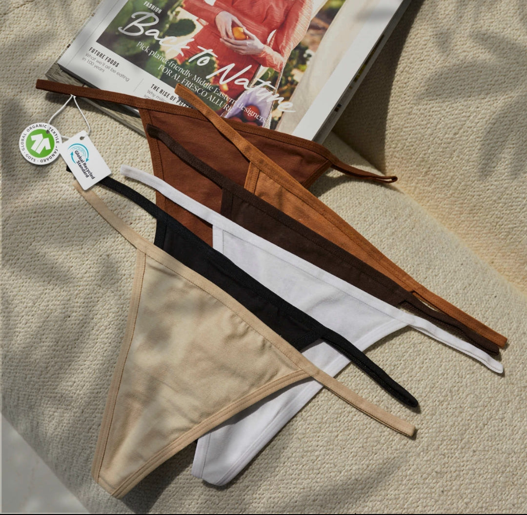 String Nix seamless thong underwear in assorted neutral shades, with sustainability tags, displayed on a magazine and fabric surface